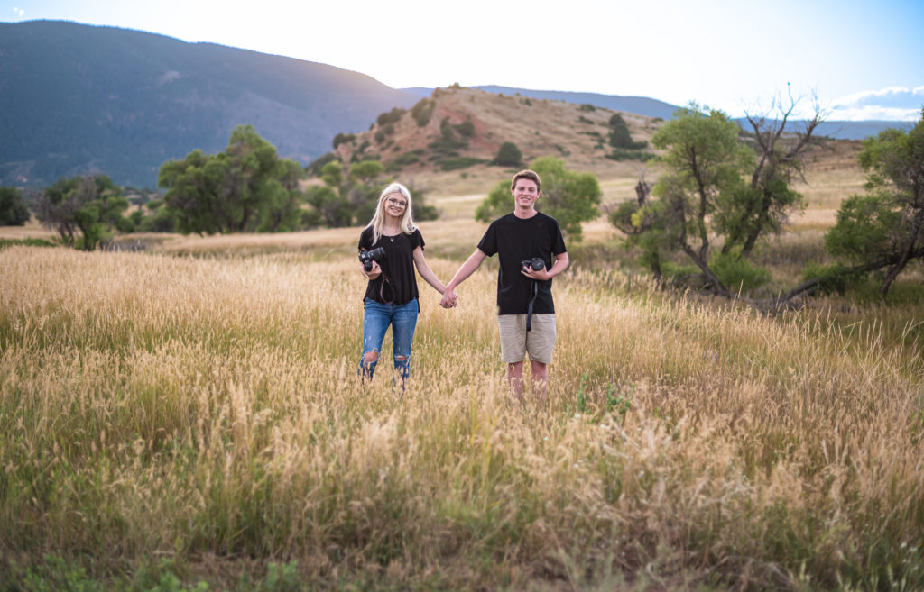A wedding photographer and videographer couple holding hands in an open field