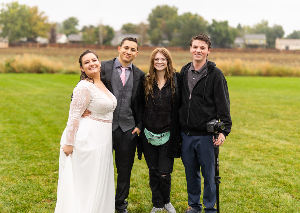 A wedding photographer and videographer with a bride and groom in an open field