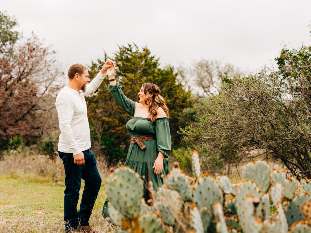 A couple dances during a family session at Pace Bend Park in Austin, TX. There is a cactus visible in the foreground of the image.