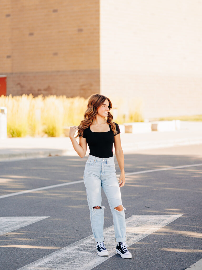 A senior wearing a black shirt and light blue jeans in Erie, CO poses at Erie High School while standing in the crosswalk.