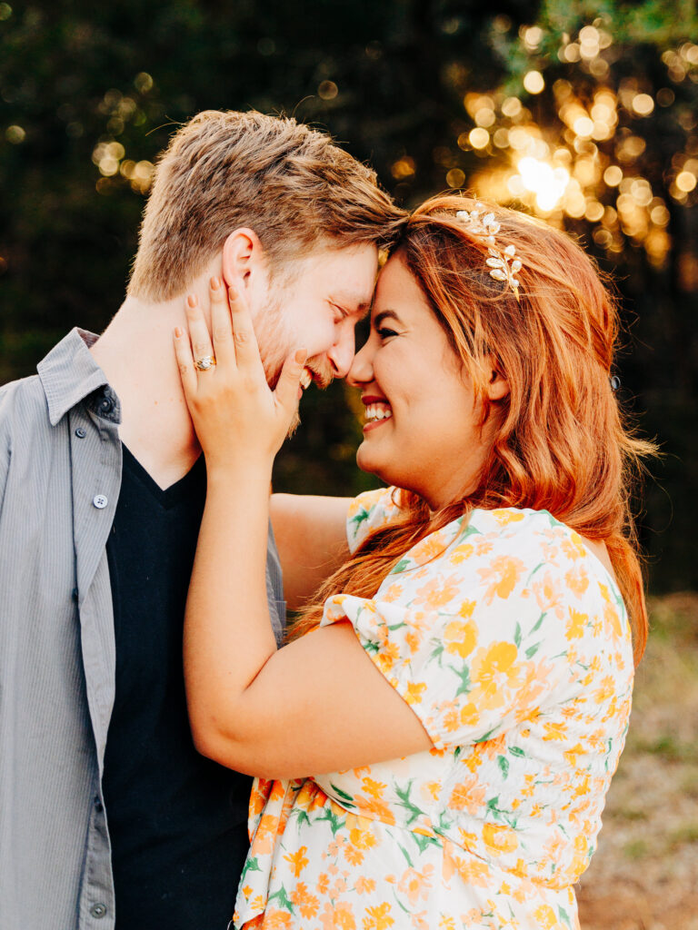 This image, taken by wedding photographer KD Captures, features an engaged couple. The couple is touching foreheads and smiling. The woman is holding the man's face. The image was taken at Diamond Barrel wedding venue.