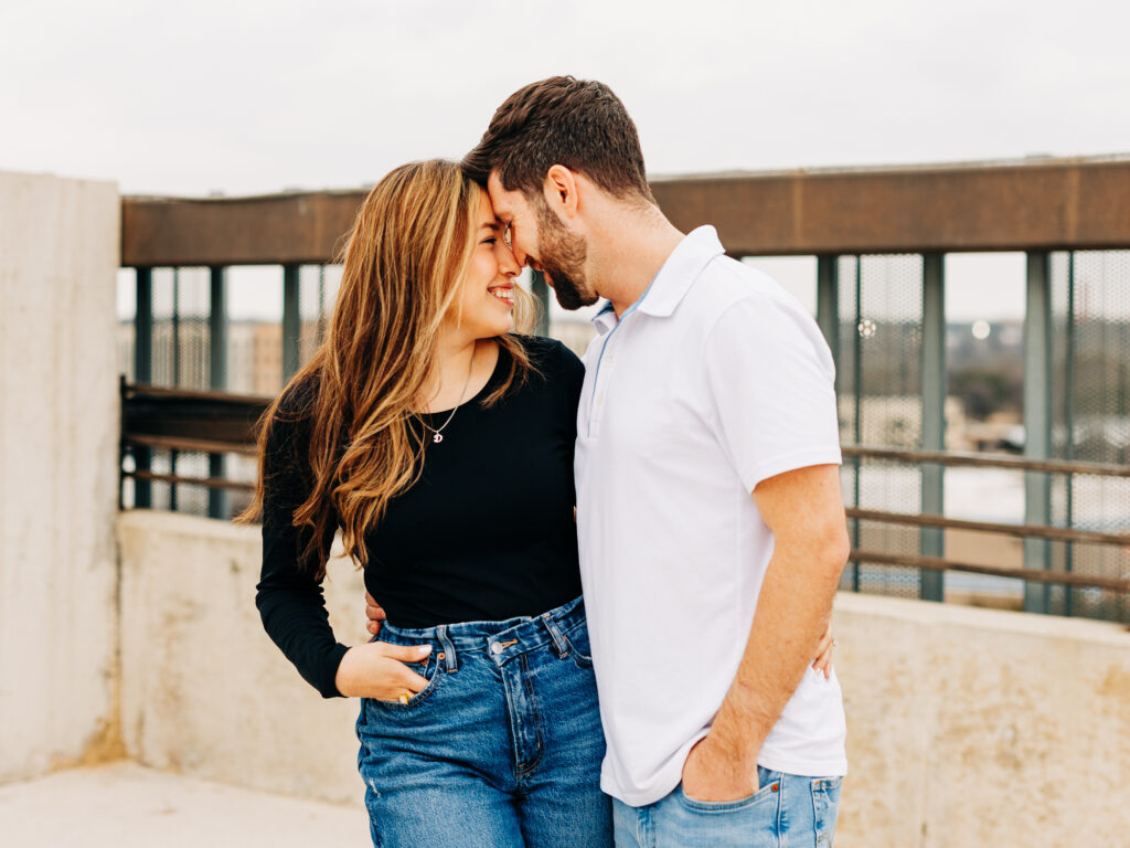A couple standing in a parking garage in San Antonio, TX. The couple is facing each other and pressing their foreheads together. 