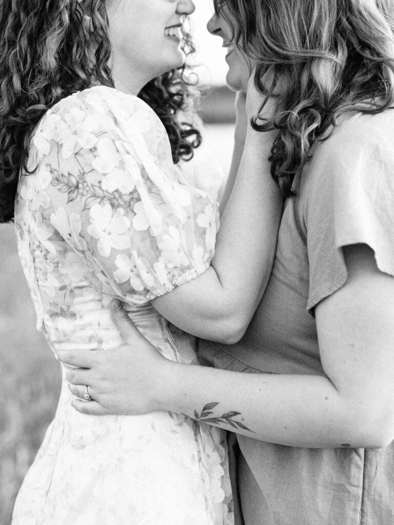 A monochrome engagement photo of two engaged women. They are facing towards eachother and holding eachother close. They are smiling and giggling in the photo.