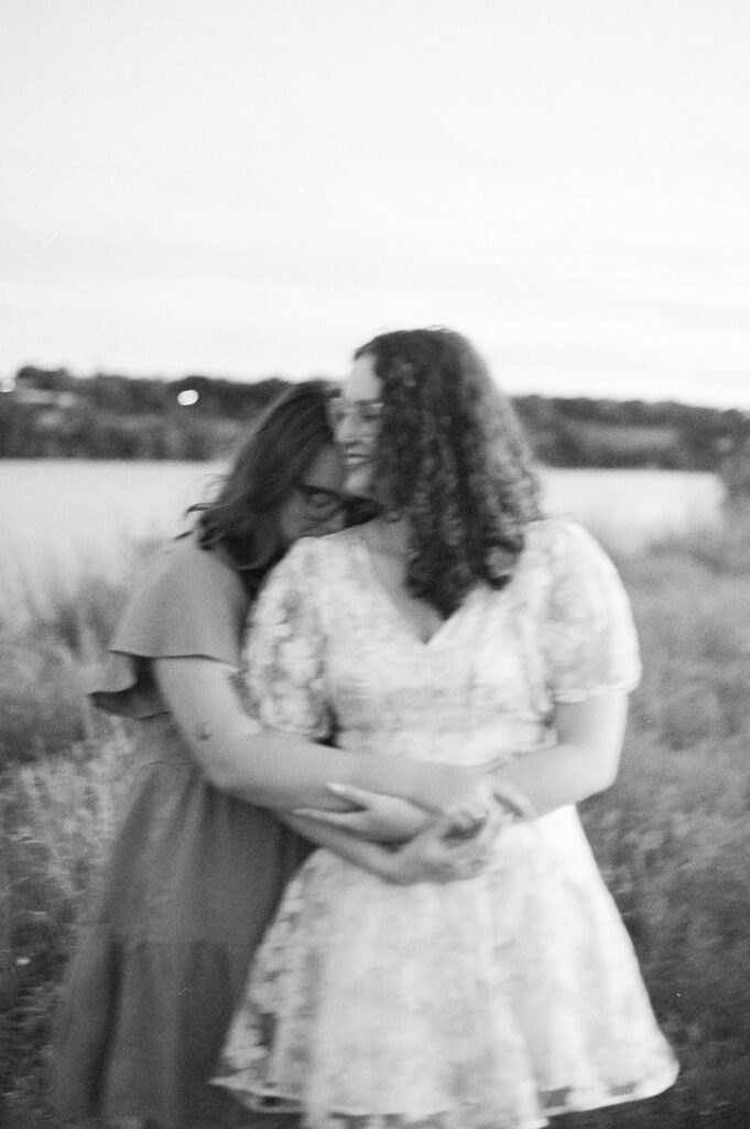 Two soon to be brides snuggling in front of a lake in Austin, Texas during their engagement photo session, taken on film