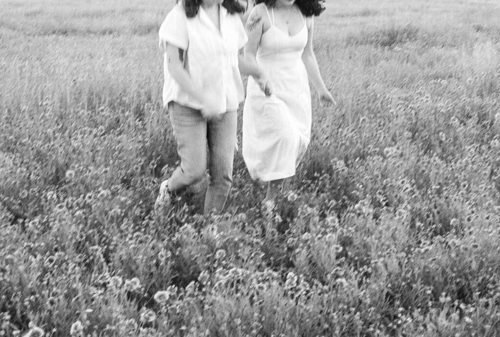 two soon to be brides running through a field of flowers in Austin, Texas during their engagement photography session. taken on film and displayed in monochrome