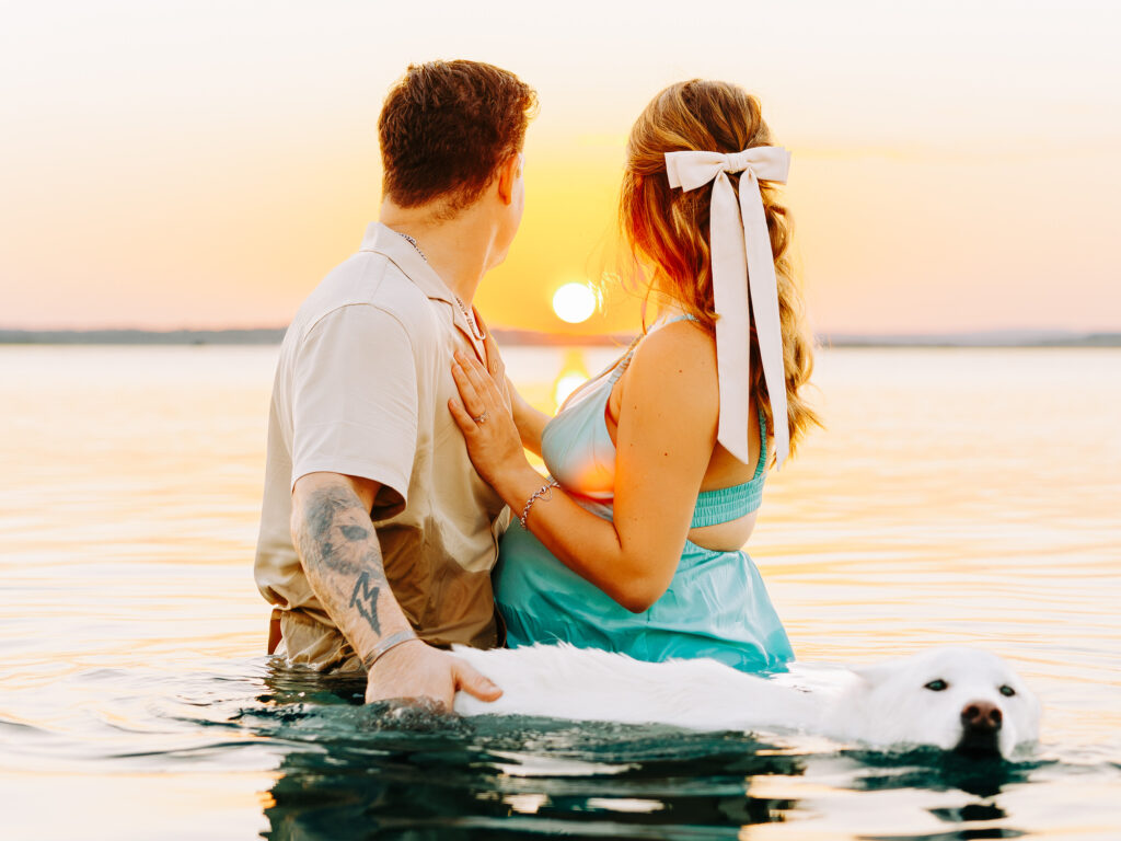 A peaceful shot of the couple standing in Canyon Lake at sunset, facing the horizon while holding their dog, creating a serene silhouette against the setting sun.