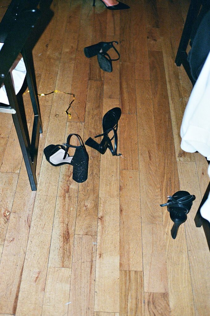 Several pairs of black high-heeled shoes are scattered across a wooden floor. Parts of tables and a white tablecloth are visible at the edges of the image.