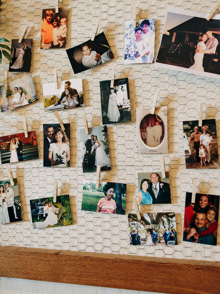 A display of various family photographs attached with clothespins to a wire grid on a wall. The photos show people at different life events, including weddings, outdoor activities, and family portraits.