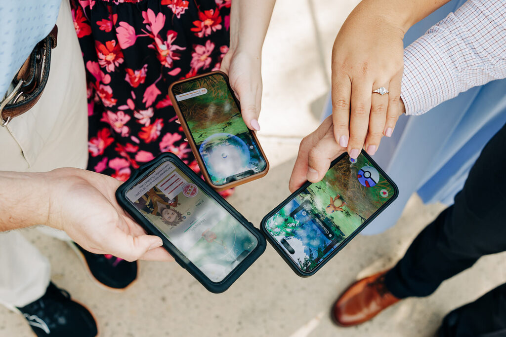 Four people stand in a circle at Natural Bridge Caverns, holding smartphones with Pokémon Go open. One wears a floral dress, and another reveals a diamond ring—capturing the excitement of a proposal from above.